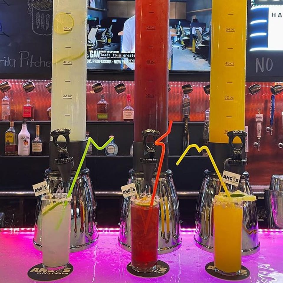Three margarita towers, lime, red, and yellow, with matching drinks on a glowing bar at Angus Grill & Cantina.