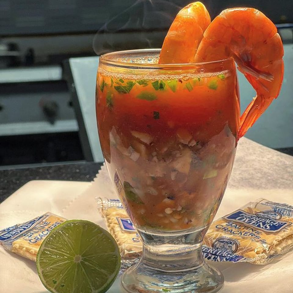 Mexican shrimp cocktail in a glass with lime and saltine crackers on a white napkin.