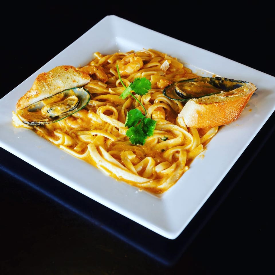 Seafood pasta with mussels, shrimp, and garlic bread on a white square plate.