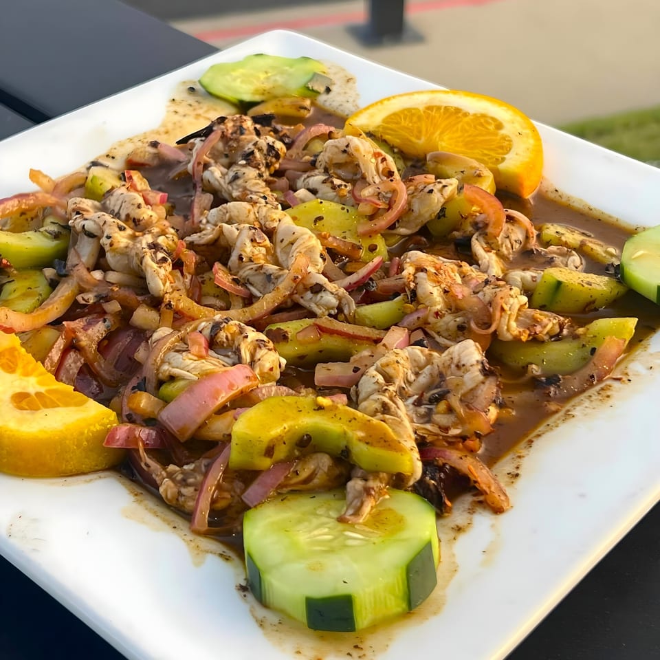 Mexican ceviche with shrimp, red onions, cucumber, and orange slices on a white plate.